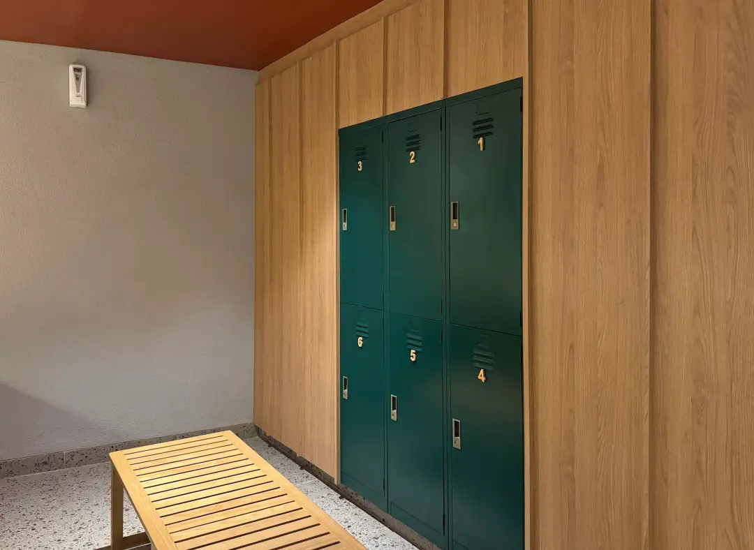 Changing room with green lockers and a timber bench